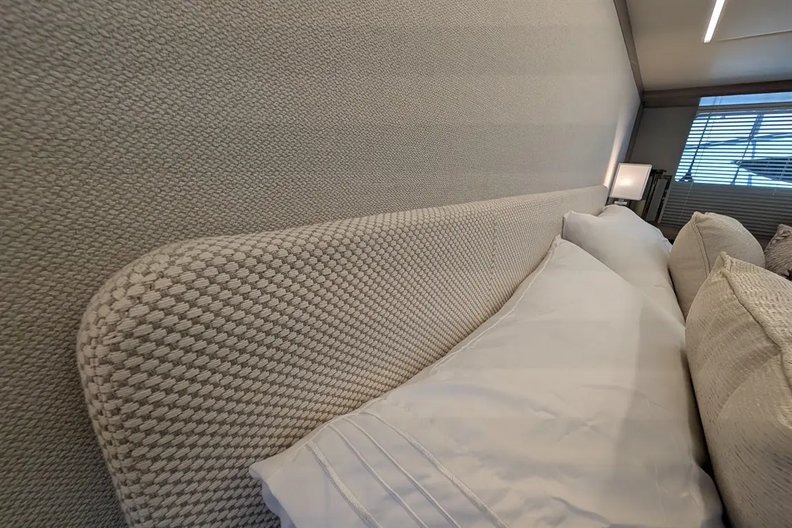 A close-up of a textured bedhead against a beige wall, featuring neatly arranged white pillows. Soft lighting enhances the interior.